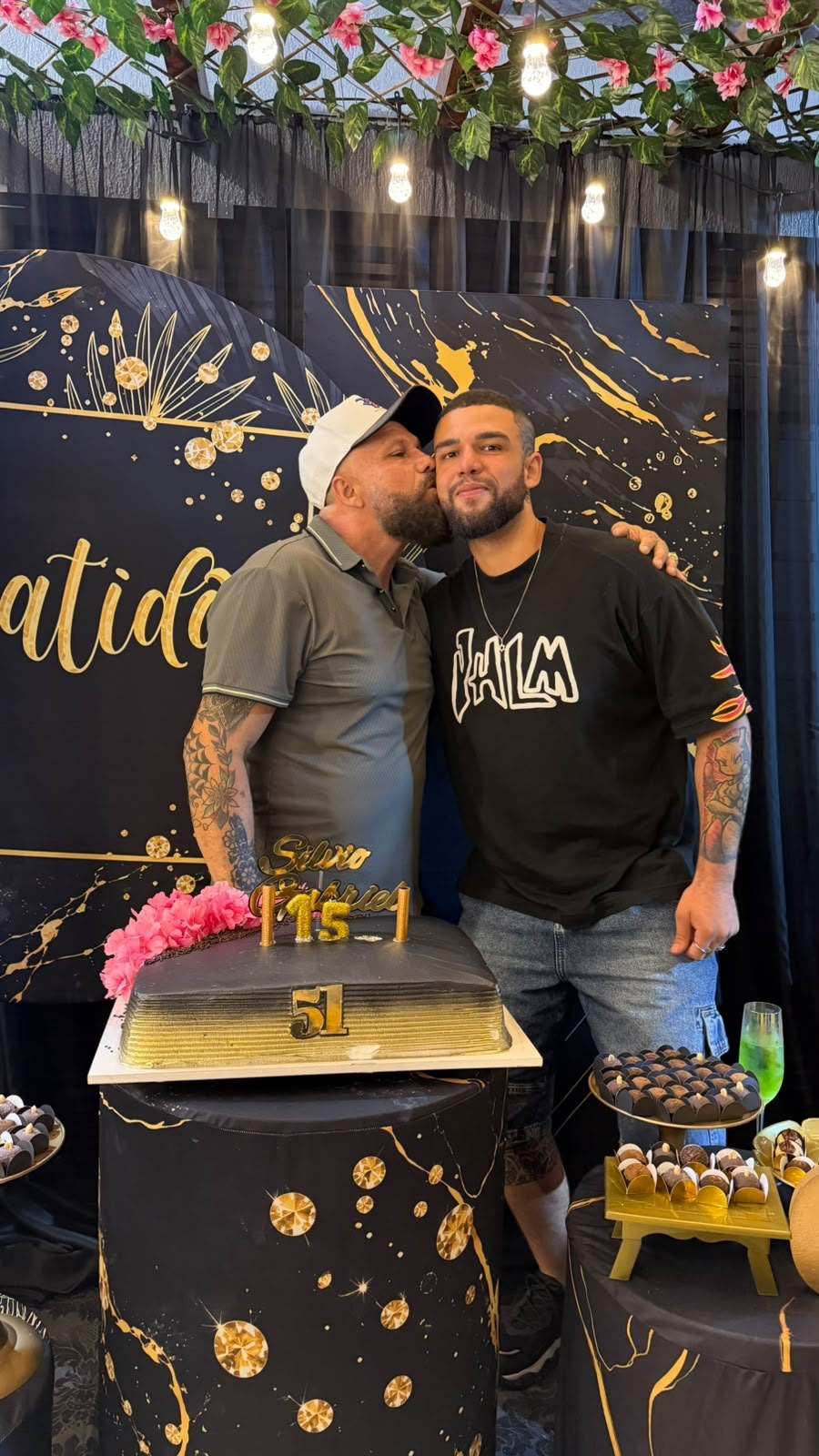 Convidados abraçados ao lado da mesa do bolo de aniversário