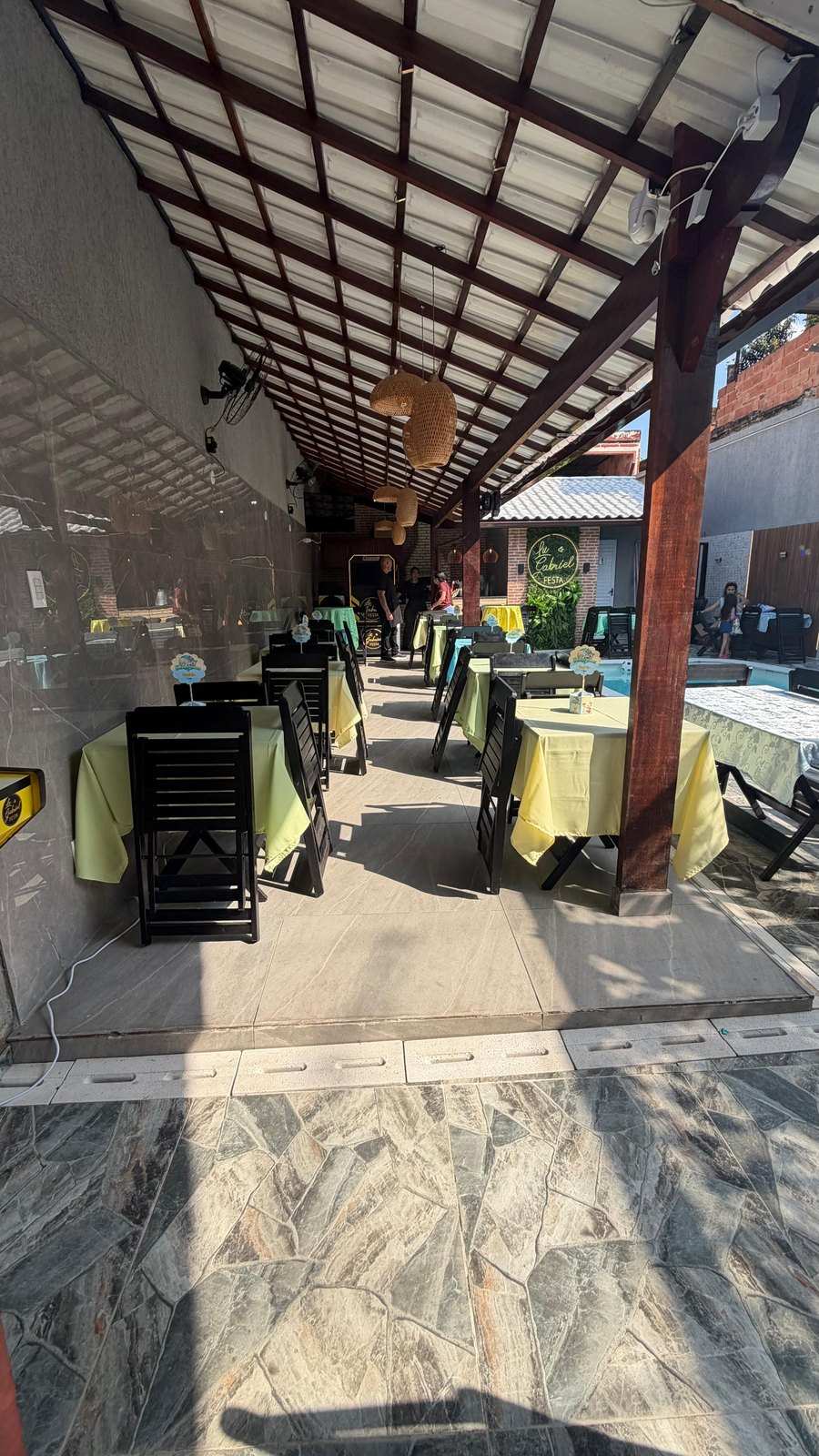 Área coberta com mesas e toalhas coloridas preparada para uma festa infantil