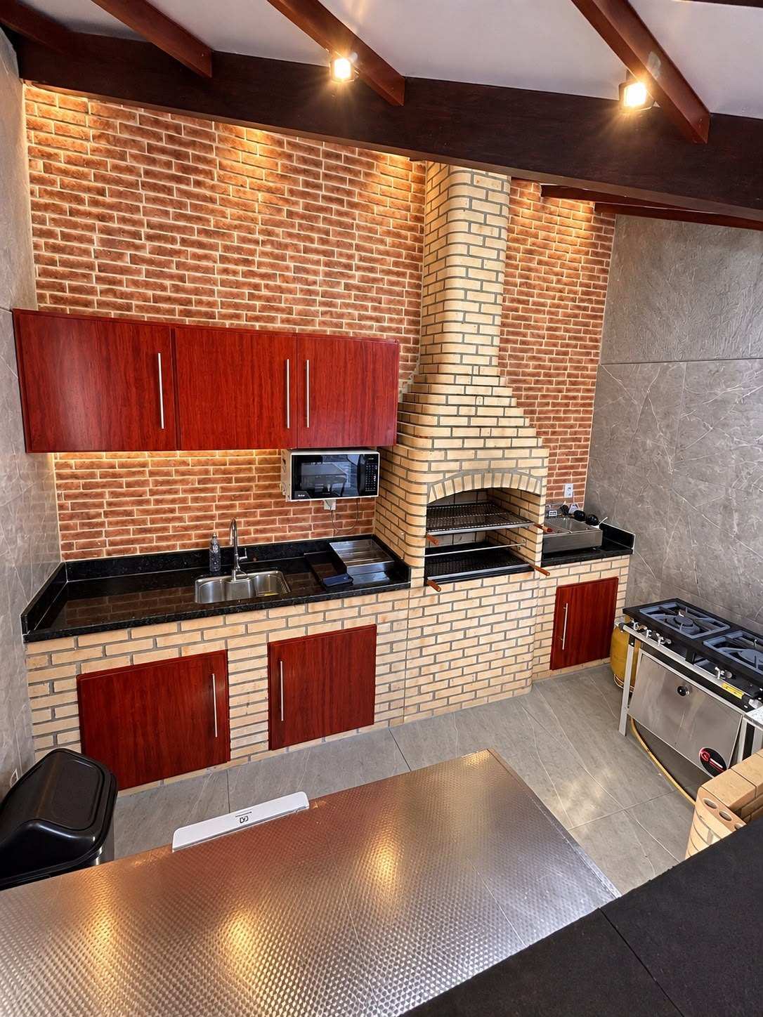 Cozinha com churrasqueira de tijolinho, armários, pia com bancada de granito, micro-ondas e fogão industrial com forno